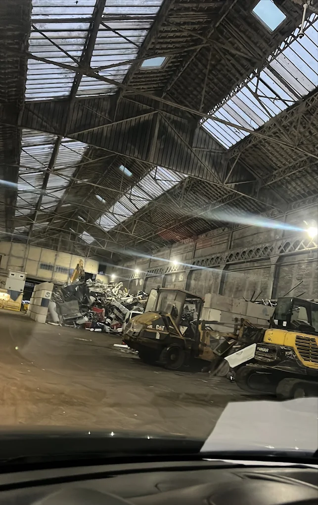 Une chargeuse et une pelle sous une grande halle, devant un tas de métaux