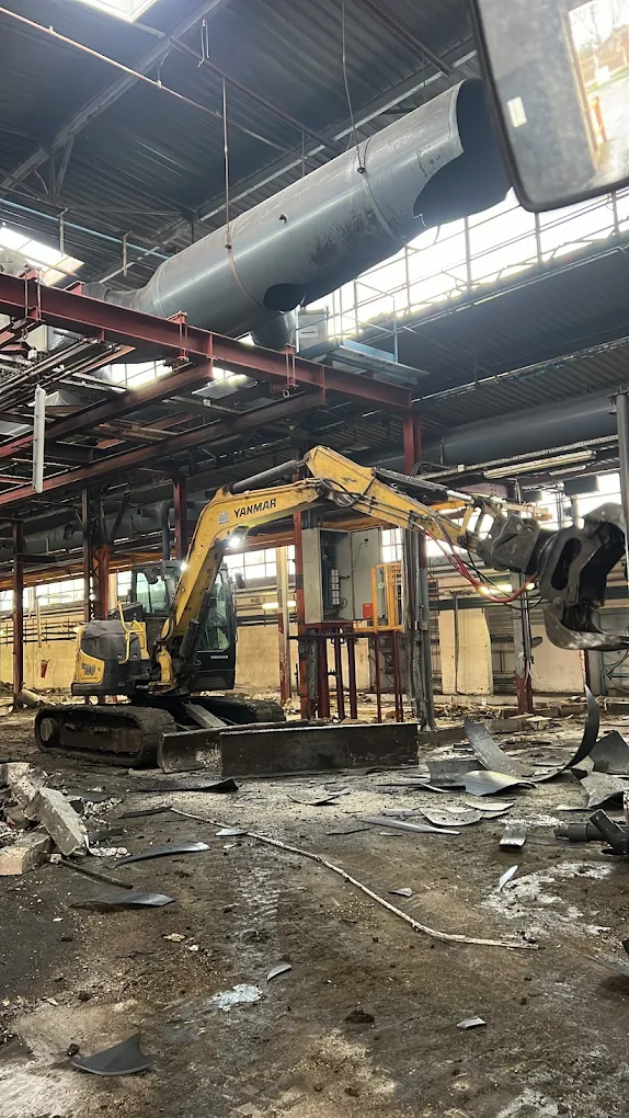 Une pelle équipée d’une pince découpe des gaines dans un hall d’usine